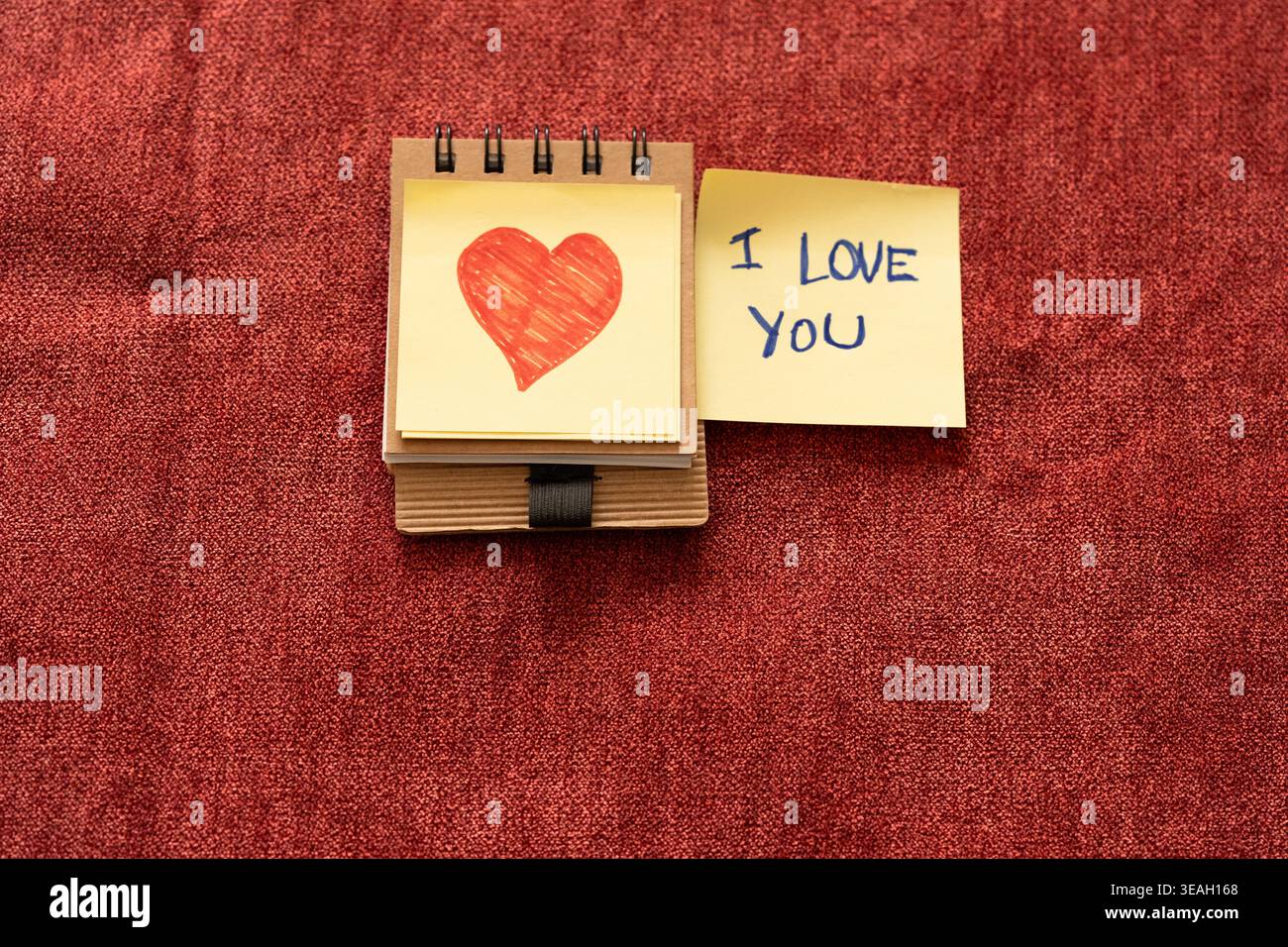 „I Love You“ handgeschriebene Notiz und handgezeichnetes Herz auf Haftnotizen über rotem Stoff Stockfoto