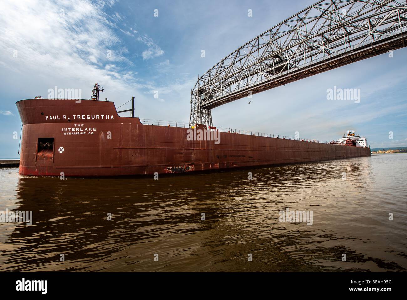 Massives Rotes Frachtschiff, Das Unter Der Steel Lift Bridge Auf Dem Calm Waterway In Der Nähe Von Shore Vorbeifährt Stockfoto