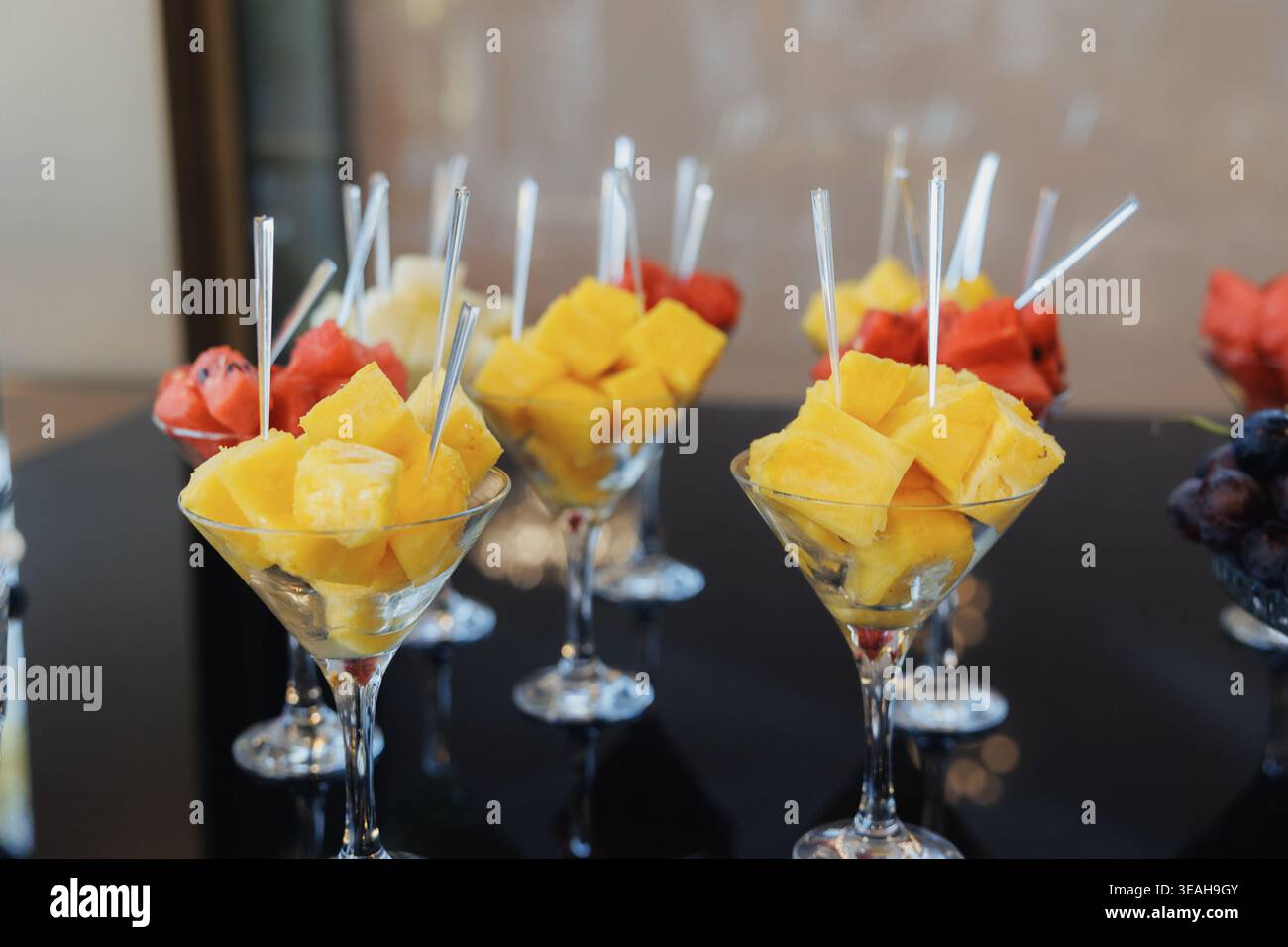 Frische Ananas- Und Wassermelonenspieße In Stielgläsern Auf Schwarzem Buffettisch, Lebhafte Tropische Farben, Cocktailgabeln, Perfekt Für Den Sommer Stockfoto