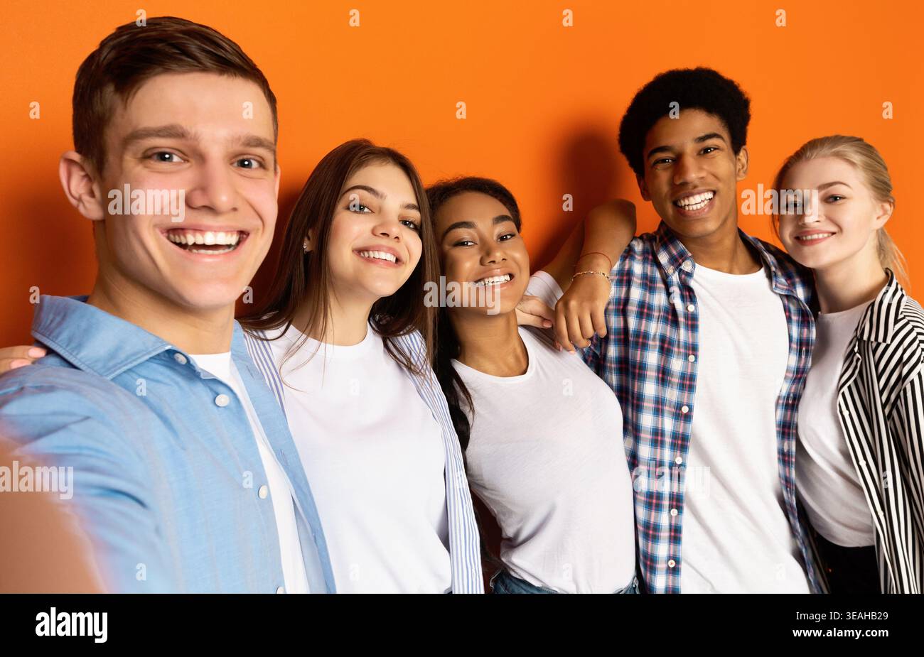 Gruppe von Freunden, die einen fröhlichen Moment zusammen vor einem orangefarbenen Hintergrund genießen Stockfoto
