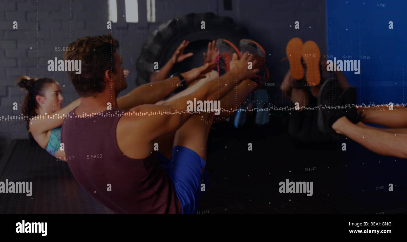 Der darstellende Mann trägt ein kastanienbraunes Tanktop und blaue Shorts, der V-Sit auf dem Fitnessboden hält, Traktorreifen Stockfoto