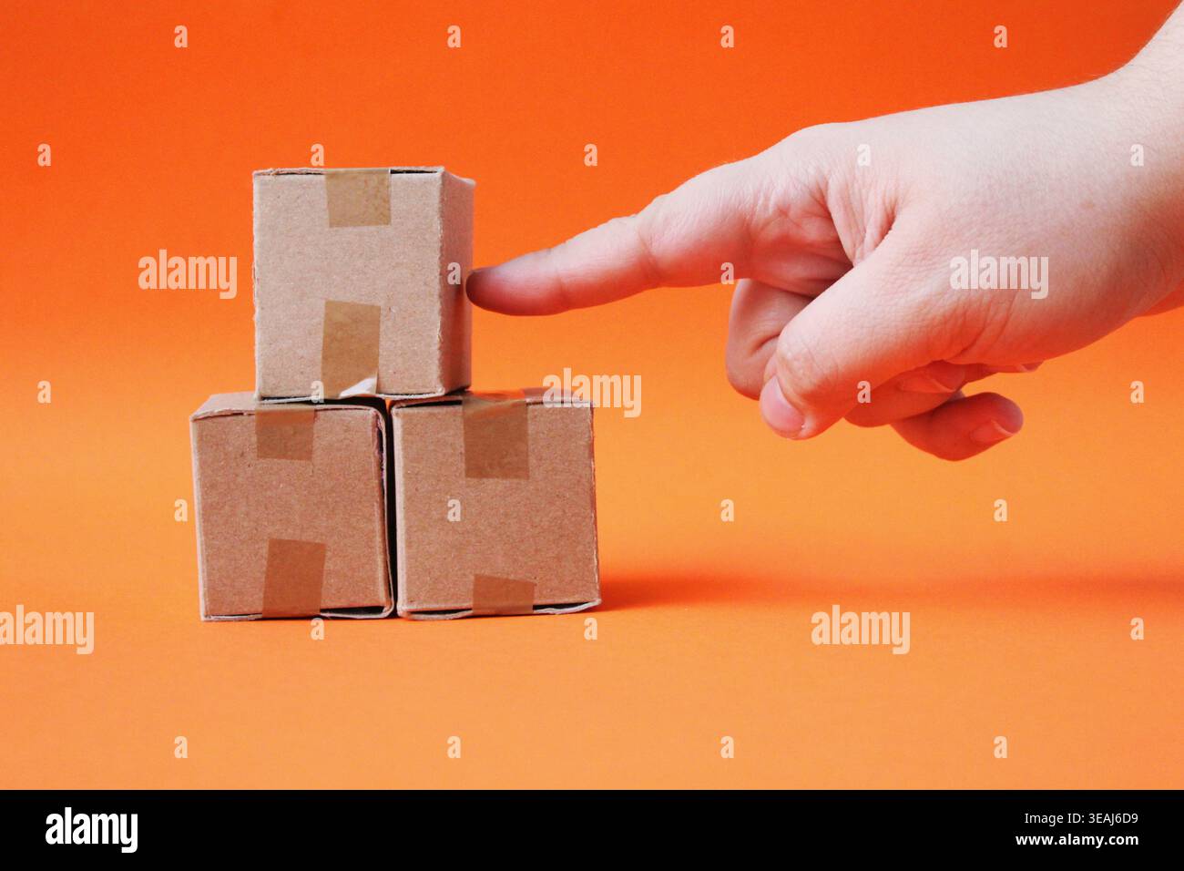 Miniatur-Box (Paket), die Teil einer Pyramide von Miniatur-Kartonschachteln mit braunem Klebeband ist, auf unendlichem orangefarbenen Hintergrund. Stockfoto