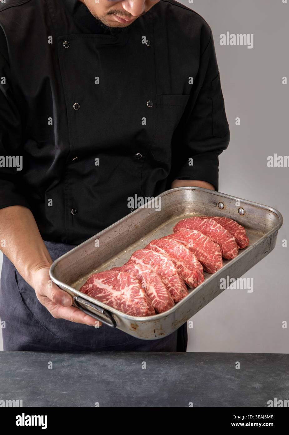 Ein Koch hält eine Pfanne rohe Rindersteaks bereit, die zubereitet werden können. Stockfoto