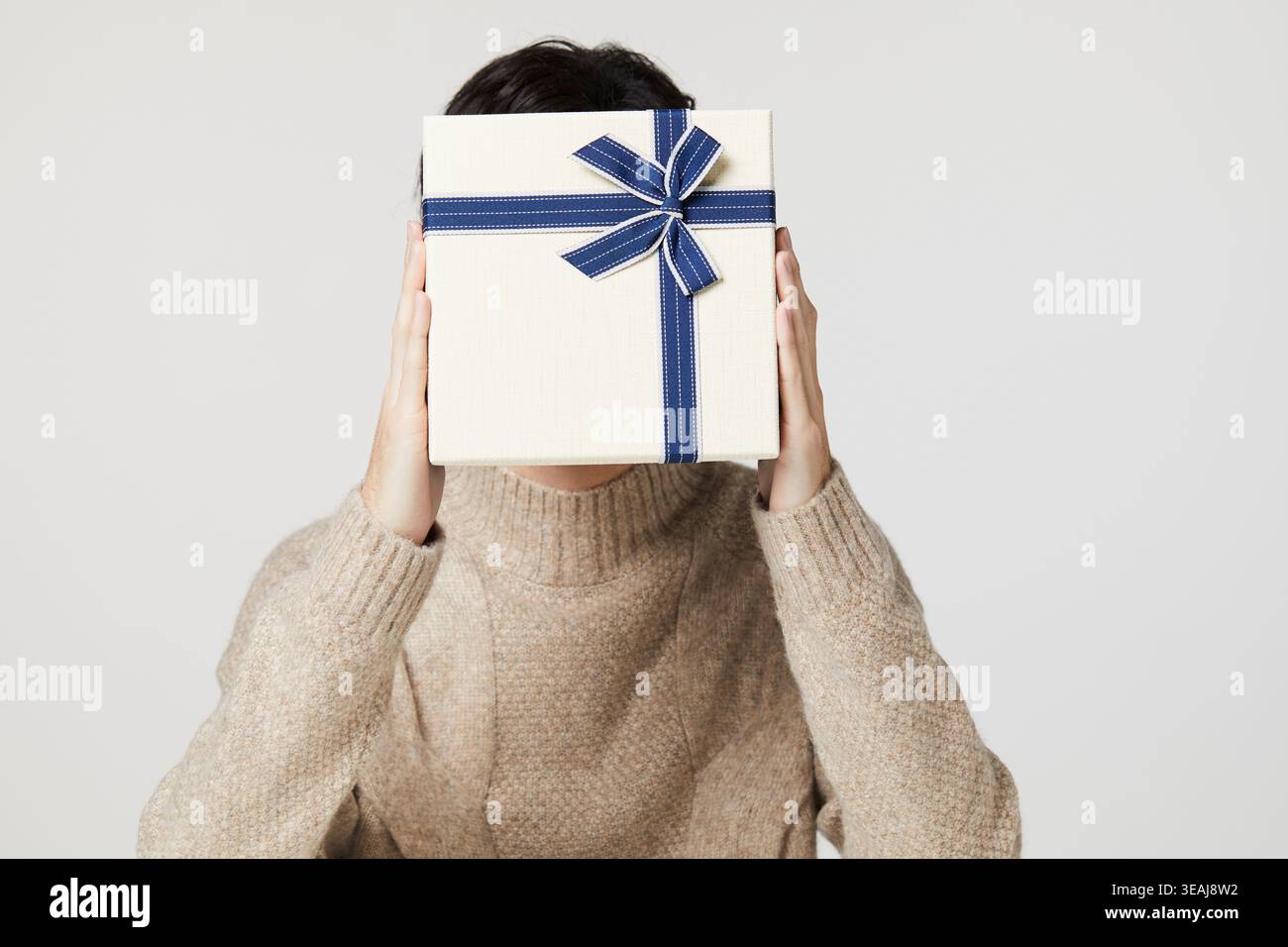 Eine junge Frau hält eine Geschenkverpackung vor ihrem Gesicht, ihre Augen hinter dem Geschenkpapier versteckt. Stockfoto