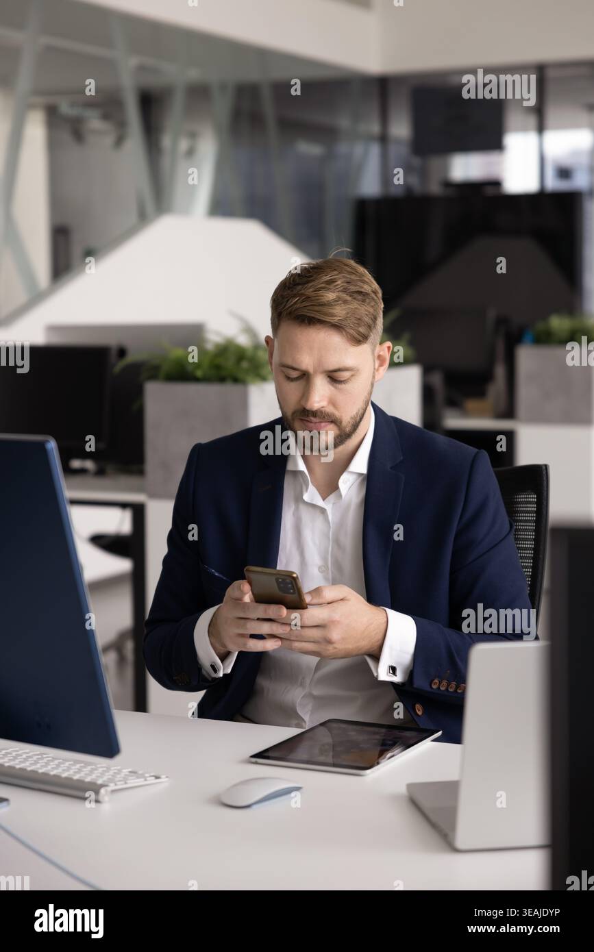 Geschäftsmann im Anzug mit Smartphone am Schreibtisch im Büro sitzen Stockfoto