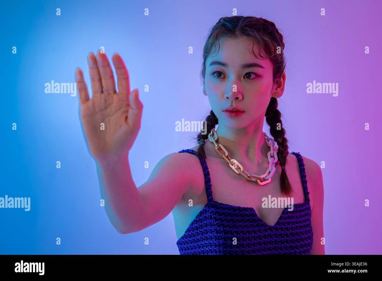 Eine junge Frau mit erhobener Hand in einer Stop-Geste vor einem lebendigen, neonbeleuchteten Hintergrund. Stockfoto