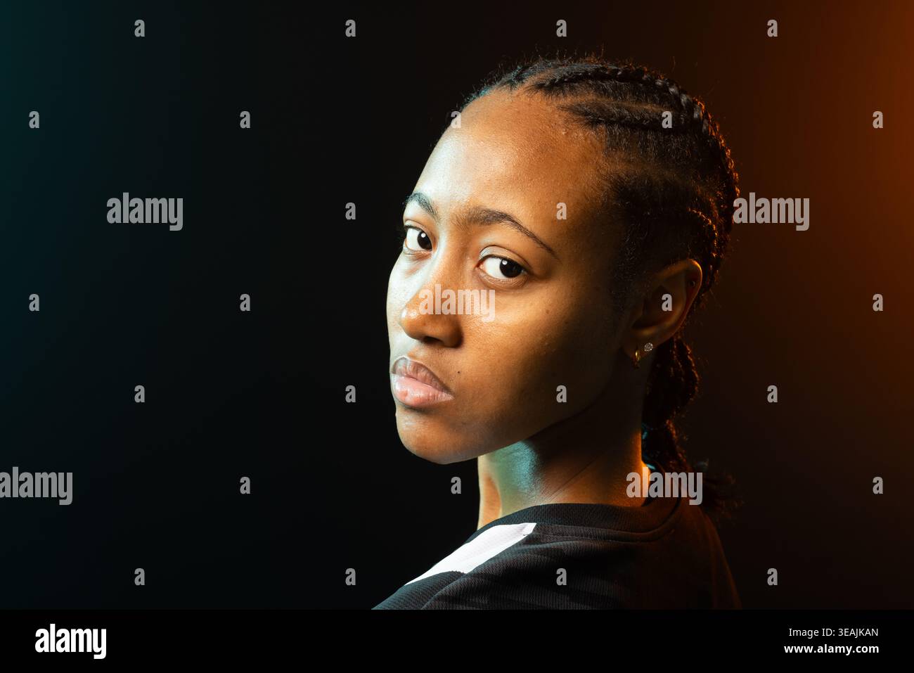 Afroamerikanerin im Studio posiert, Top mit weißem Streifen, Nieten, blaubrauner Felgenbeleuchtung Stockfoto