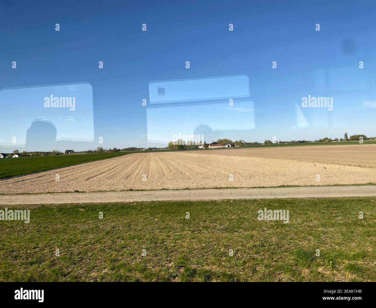 Zugfenster Blick auf das gepflügte Feld glasige Reflexion deutet auf das Innenleben der Wagen hin, breite braune Furchen Stockfoto