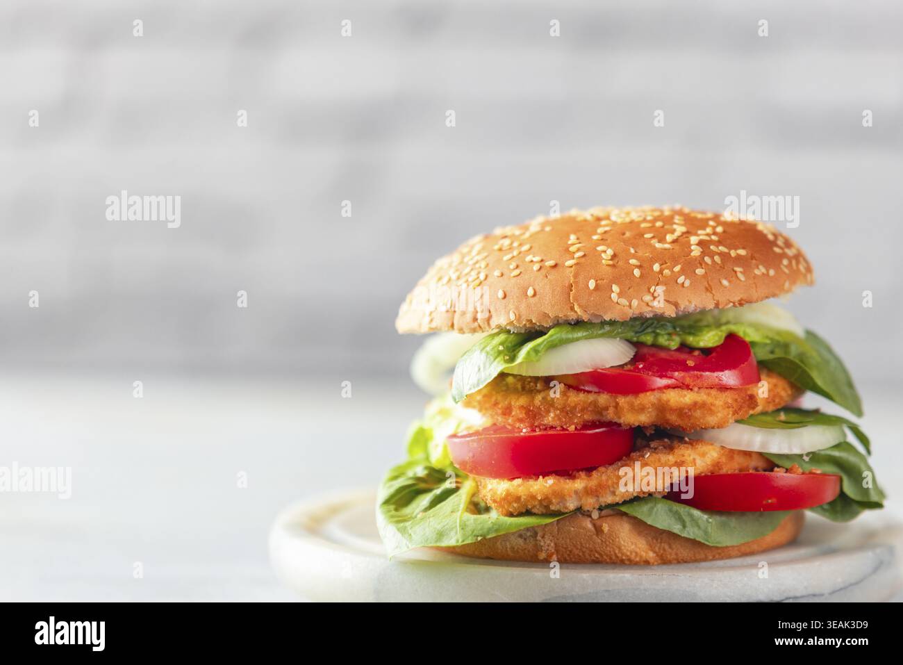 Burger mit veganem Schnitzel, Tomaten, Zwiebeln und Salat, helle Umgebung Stockfoto