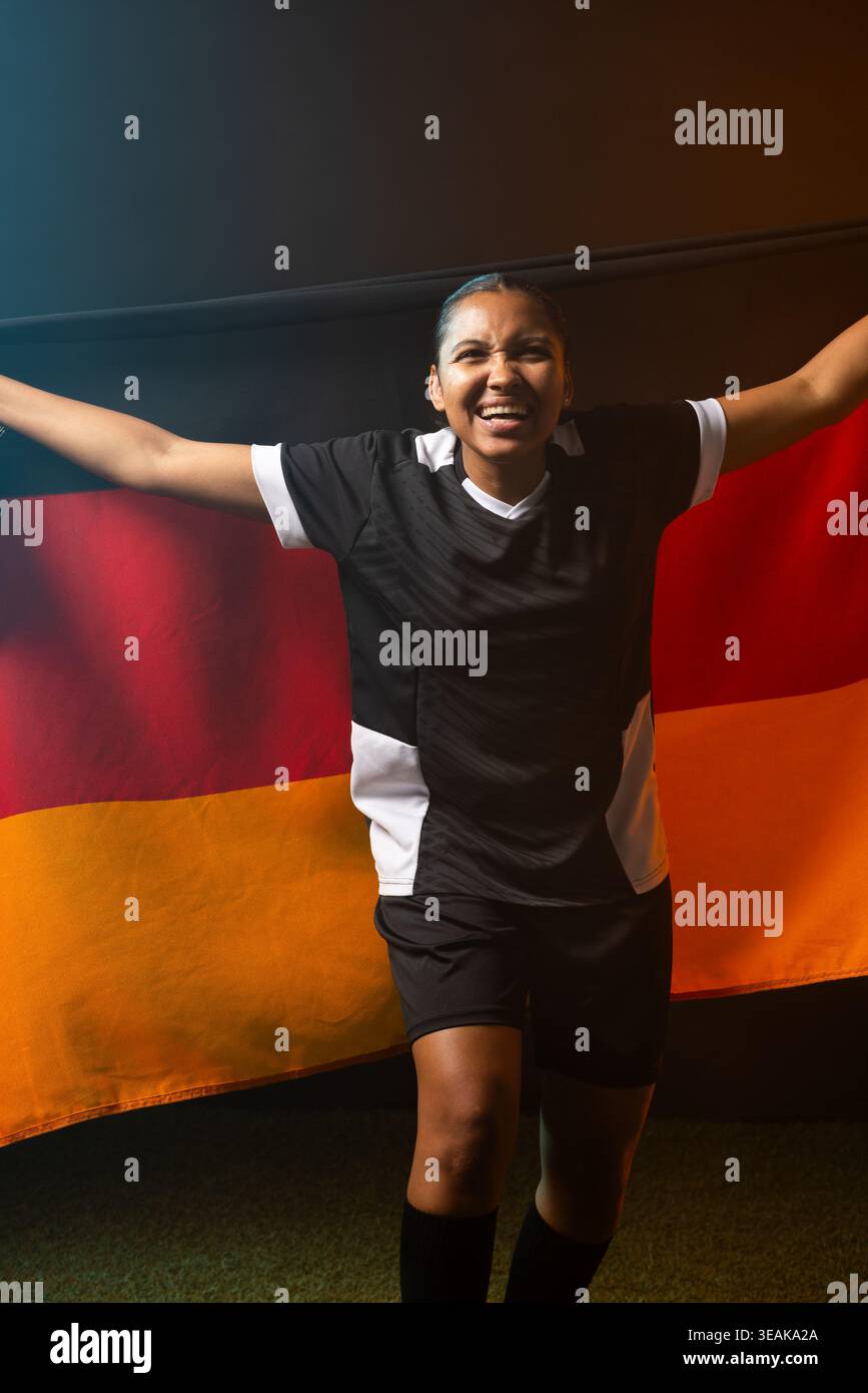 Afrikanische Athletin mit schwarz-rot-goldener Trikolore-Flagge auf grünem Rasen, mit schwarz-weißem Trikot. Spieler, Banner, Stadion, Uniform, Feier, dra Stockfoto
