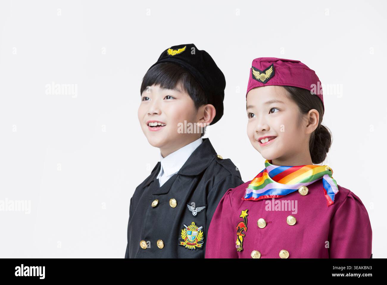 Zwei als Pilot und Flugbegleiter gekleidete Kinder stehen Rücken an Rücken und lächeln in die Kamera. Stockfoto