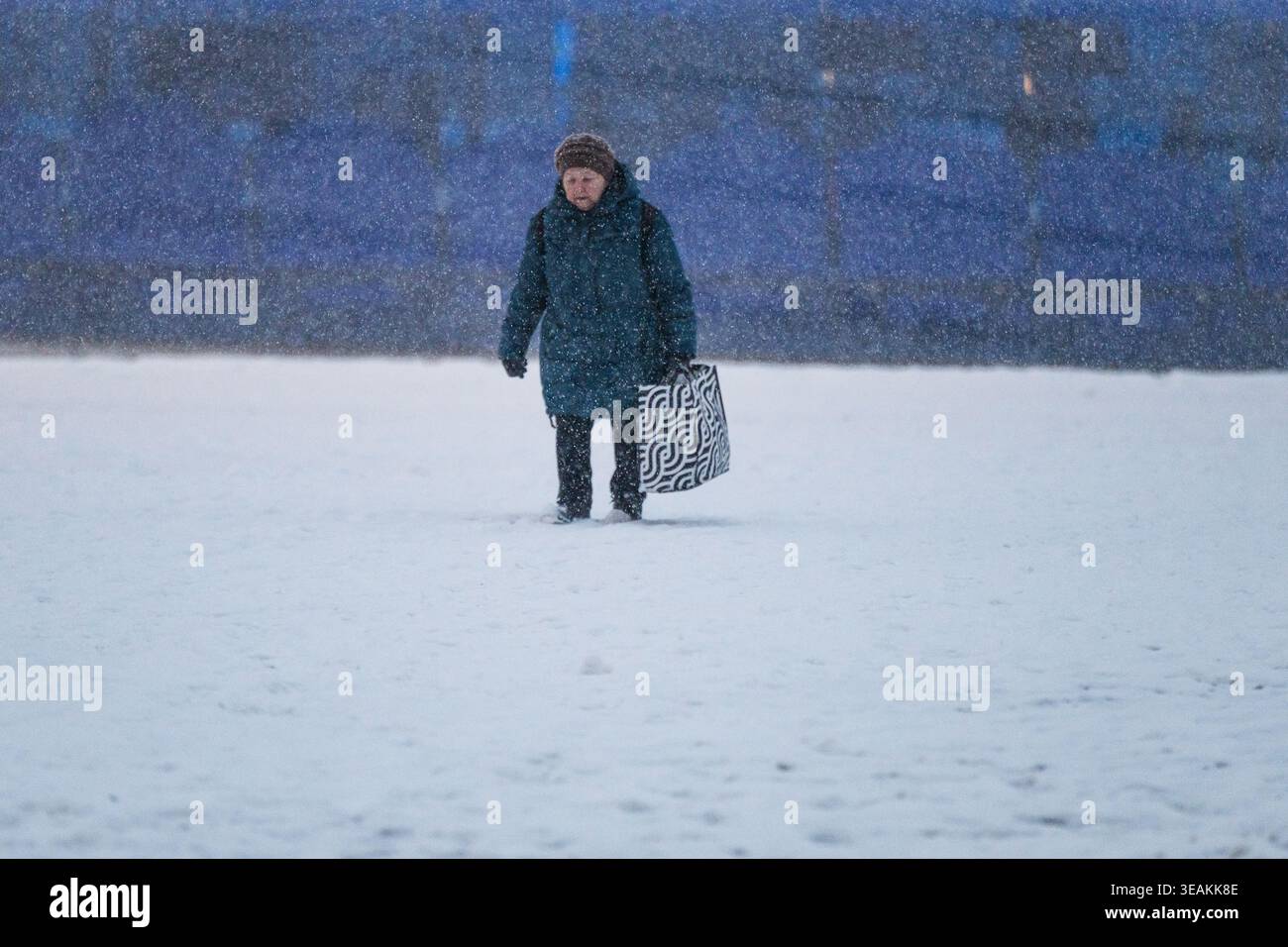 Tallinn, Estland - 03. Januar 2025: Blick auf eine Einzelfigur, die dem starken Schneefall trotzt, ein starker Kontrast zum gedämpften blauen Hintergrund der Stadt Stockfoto