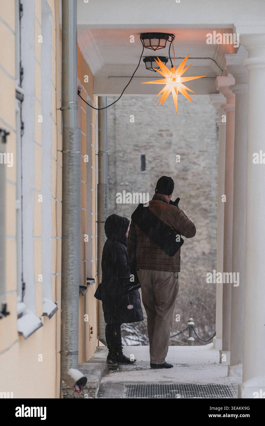 Tallinn, Estland - 03. Januar 2025: Blick auf einen Vater und ein Kind, die unter einem beleuchteten Stern stehen und auf die alten Steinmauern der Altstadt auf einem schneebedeckten Boden blicken Stockfoto