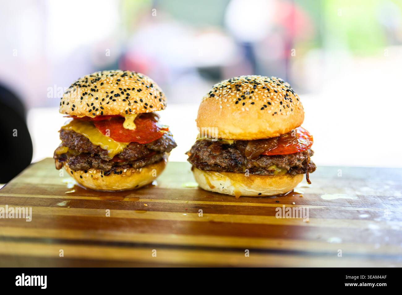 Nahaufnahme eines frisch zubereiteten Cheeseburgers mit doppelten Rindfleischpasteten, geschmolzenem Käse und Sesambrötchen auf einer Holzoberfläche, die saftig ist Stockfoto