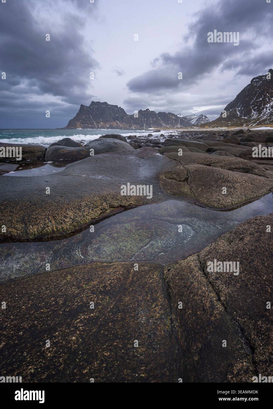 Am Uttakleiv Beach in Lofoten, Norwegen, prallen Wellen sanft auf einzigartige Felsformationen unter einem stimmungsvollen Himmel. Dieser ruhige Ort ist perfekt für Naturliebhaber. Stockfoto