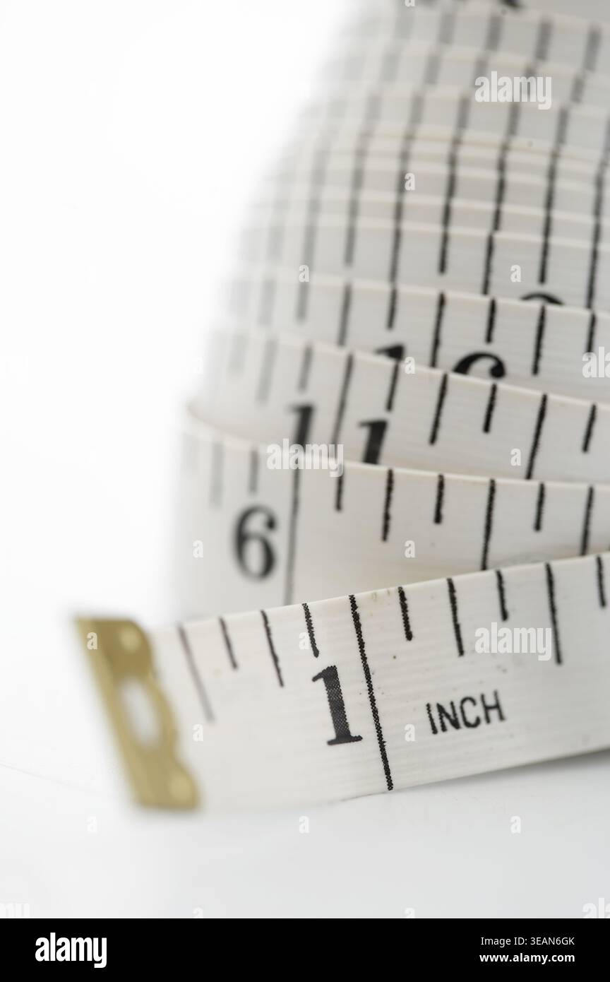 Auf einer weißen Oberfläche liegt ein weißes, gewickeltes, flexibles und präzises Maßband, das für präzise Messungen verwendet werden kann. Stockfoto