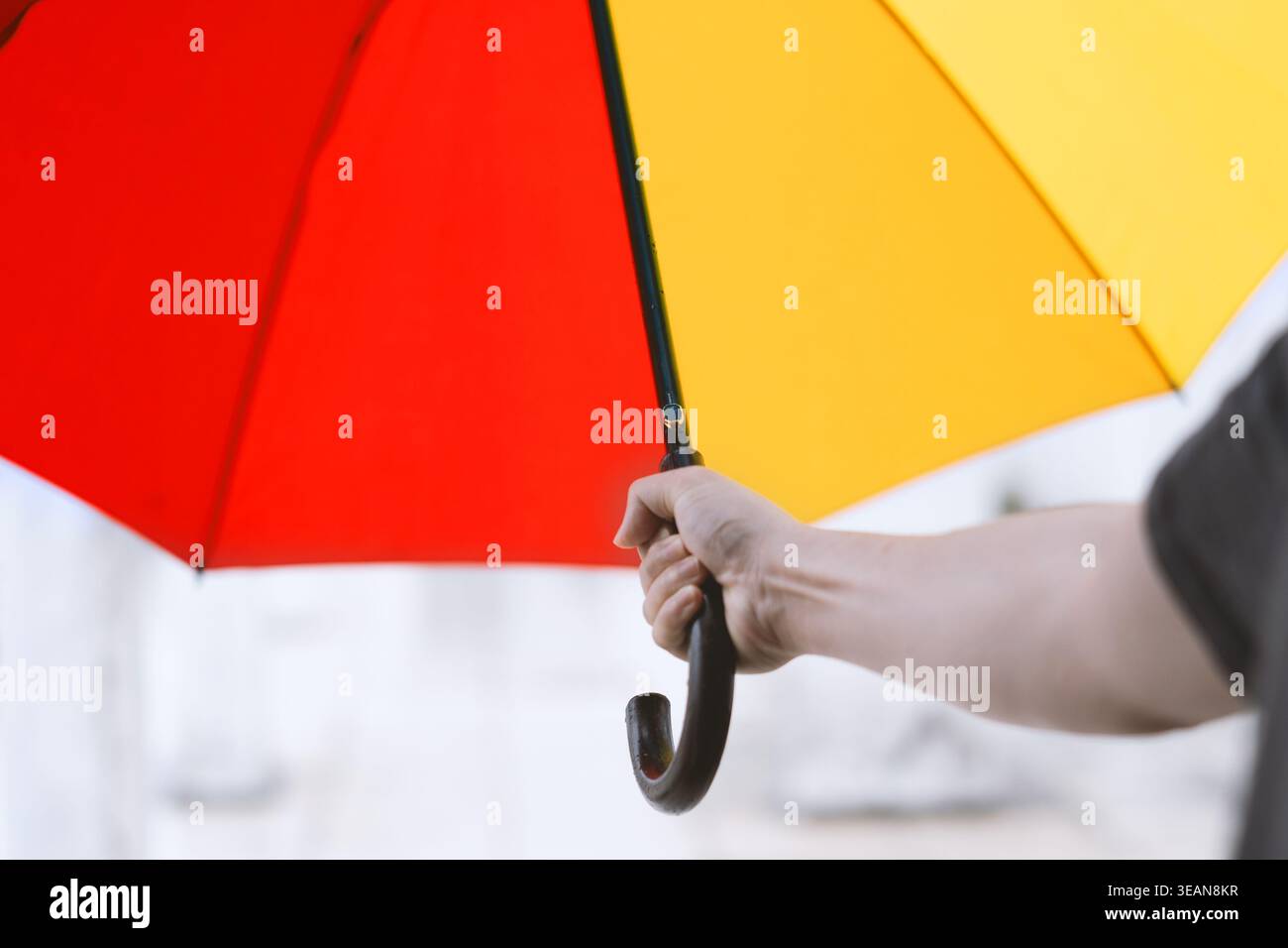 Nahaufnahme einer Hand, die einen leuchtenden rot-gelben Regenschirm vor einem verschwommenen schneebedeckten Hintergrund hält Stockfoto