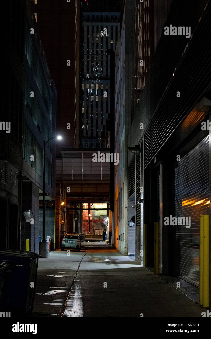 Atmosphärischer Blick auf eine enge urbane Gasse bei Nacht zwischen Gebäuden, mit geparktem Auto, stimmungsvoller Straßenbeleuchtung, Noir One Point Perspektive Stockfoto