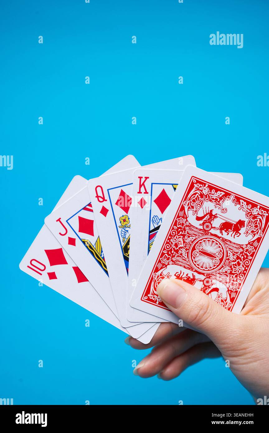 Eine Hand hält ein Standardspiel mit 52 Karten, wobei der Pik-König nach oben zeigt, vor einem hellblauen Hintergrund. Stockfoto
