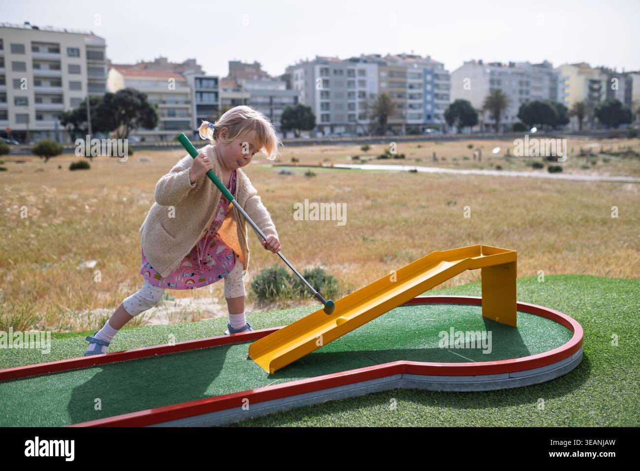 Sorglose Kindheit: Blondes Mädchen genießt einen lustigen Tag des Minigolfens in der Stadt Stockfoto
