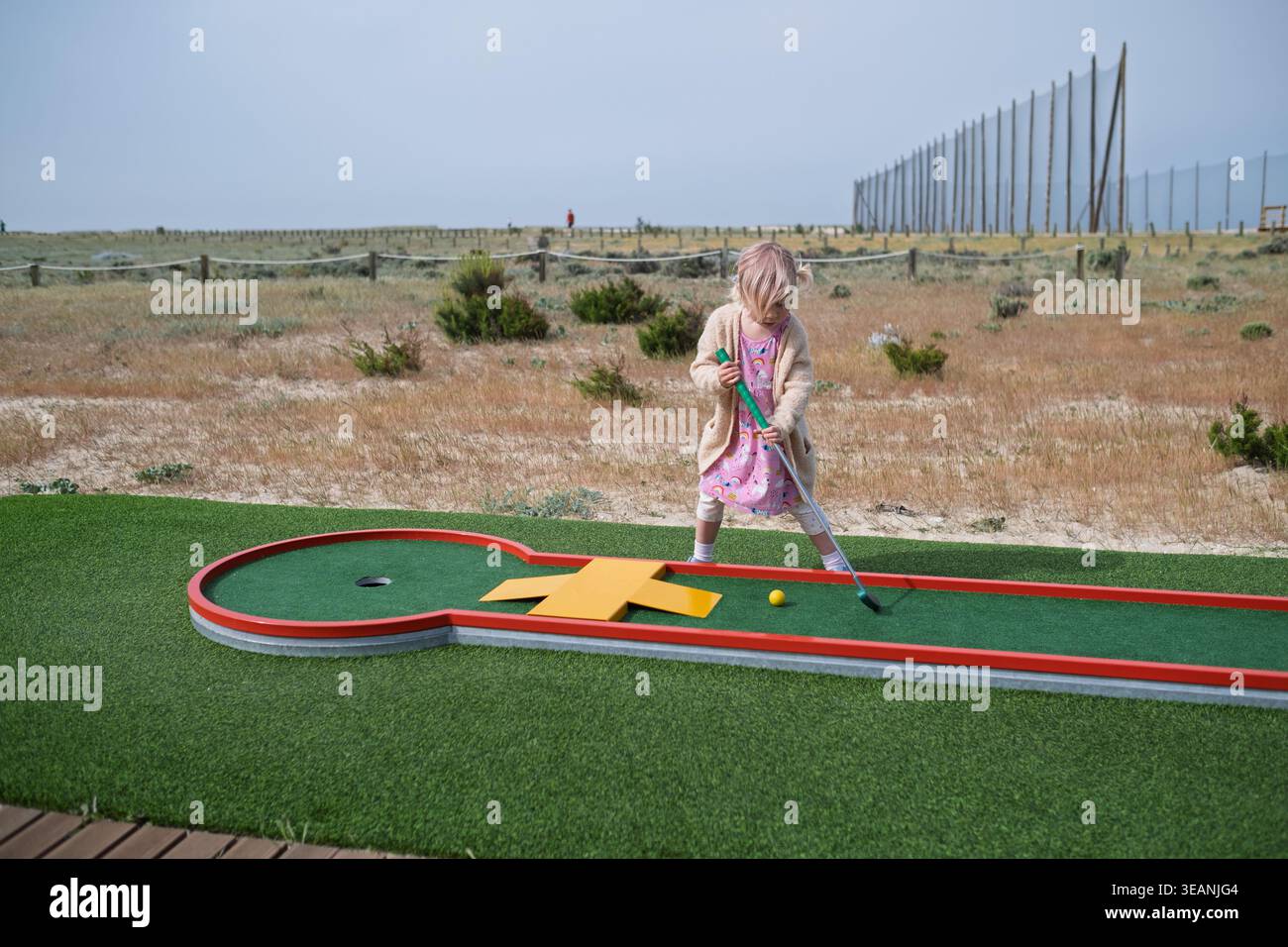 Sorglose Kindheit: Blondes Mädchen genießt einen lustigen Tag des Minigolfens in der Stadt Stockfoto