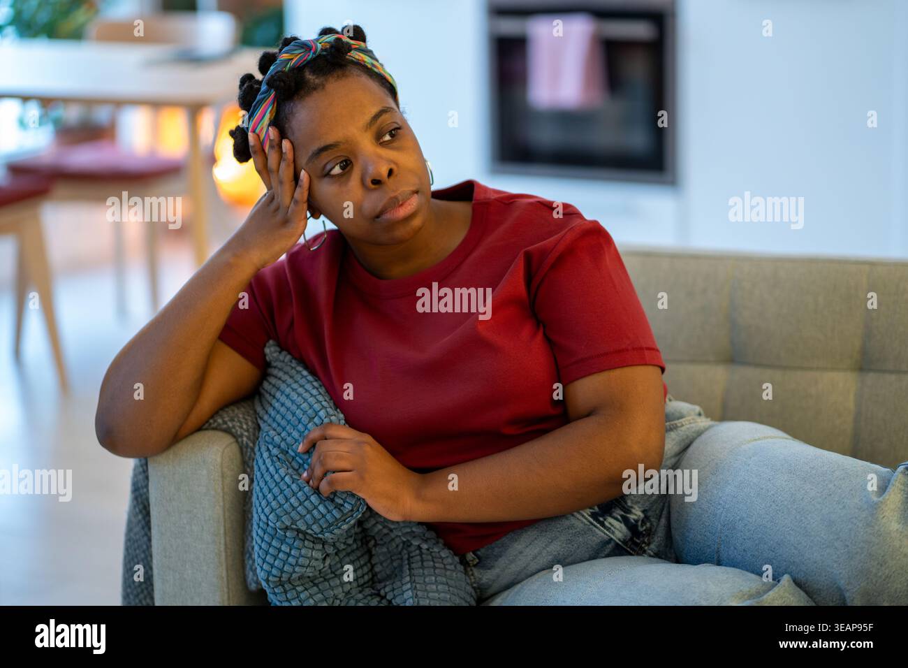 Müde frustrierte afroamerikanische Frau sitzt zu Hause auf dem Sofa und fühlt sich irritiert, verärgert, schlecht gelaunt Stockfoto