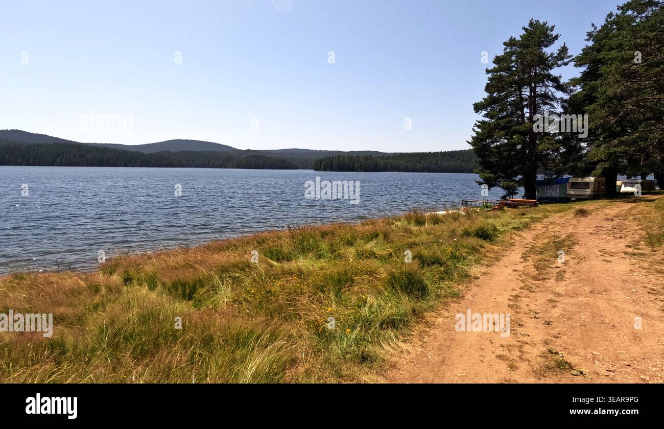 Sonniger Blick auf den See am Golyam Beglik Reservoir mit unbefestigter Straße, Kiefernwald, Campingplatz und ruhigem blauem Wasser im Spätsommer. 2023 Stockfoto