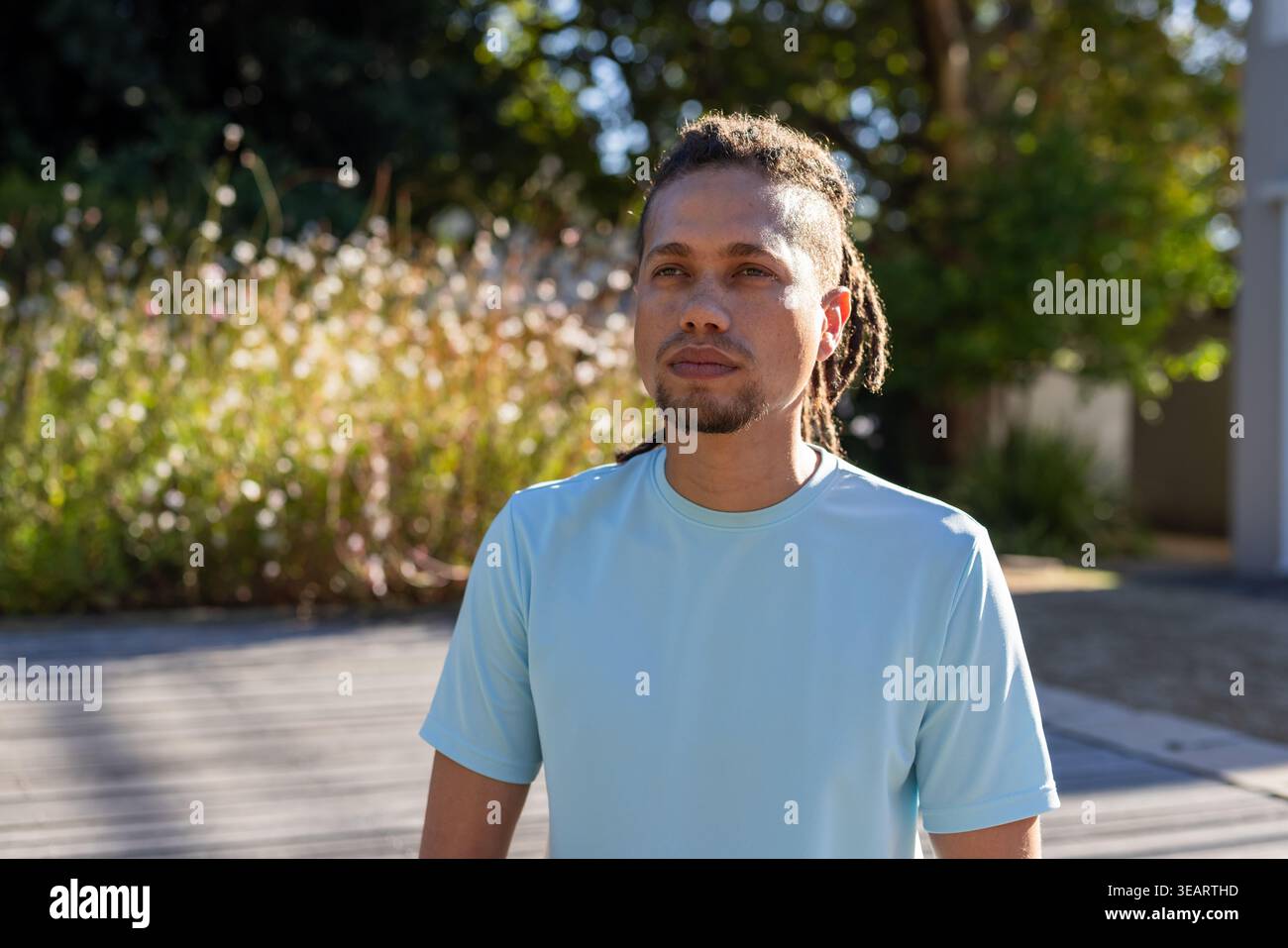 Afroamerikaner, der auf Holzdeck steht und hellblaues T-Stück trägt und auf hohe Gräser blickt. Dreadlocks, Porträt, Sonnenlicht, draußen, Promenade, Natur Stockfoto