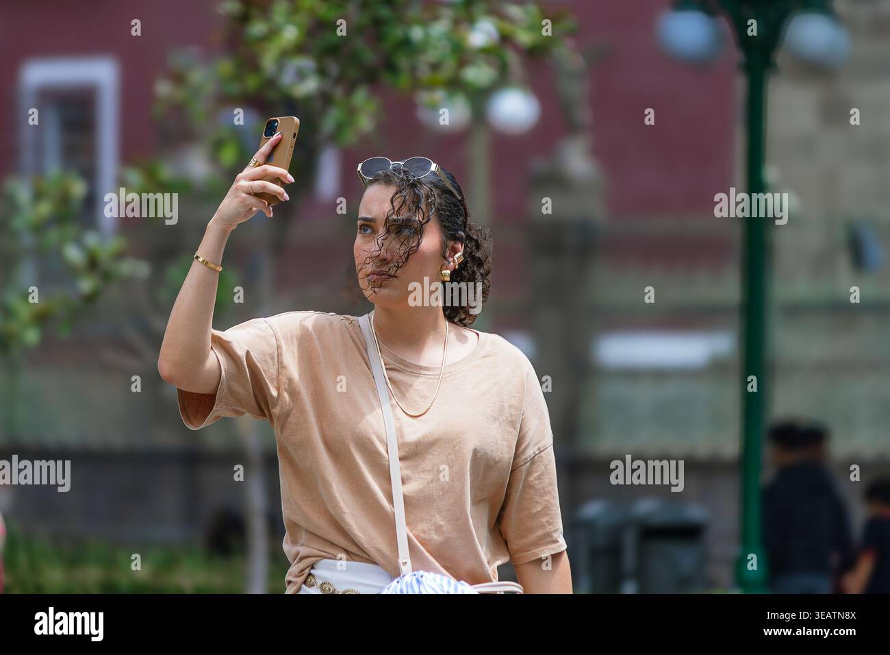 Eine junge Frau mit Sonnenbrille am Kopf hält ihr Handy hoch, um ein Foto in einem Park zu machen. Stockfoto