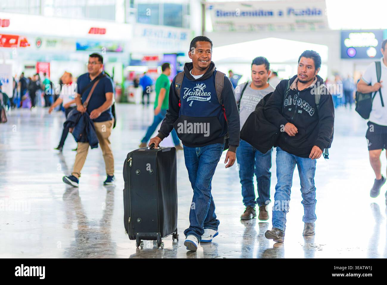 Lächelnde Männer mit Koffern und Rucksäcken fahren durch den Busbahnhof Puebla und halten einen alltäglichen Moment der Reise in Mexiko fest. Stockfoto