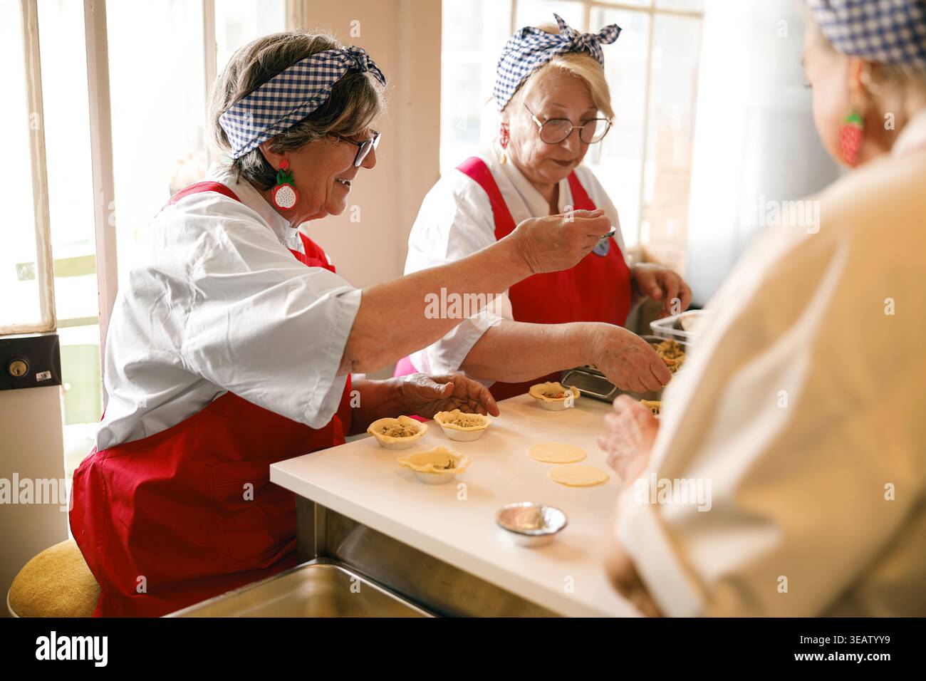 Drei Seniorinnen, die Teigkuchen zusammen in einem hellen kulinarischen Workshop füllen Stockfoto