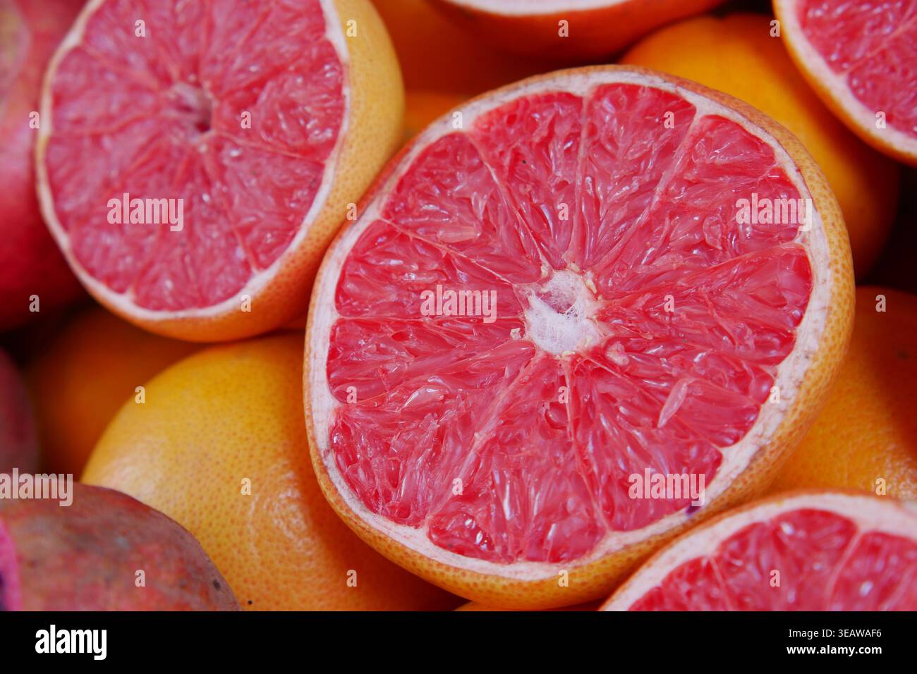 Frische Grapefruits, die in der Hälfte unter ganzen Früchten geschnitten werden Stockfoto