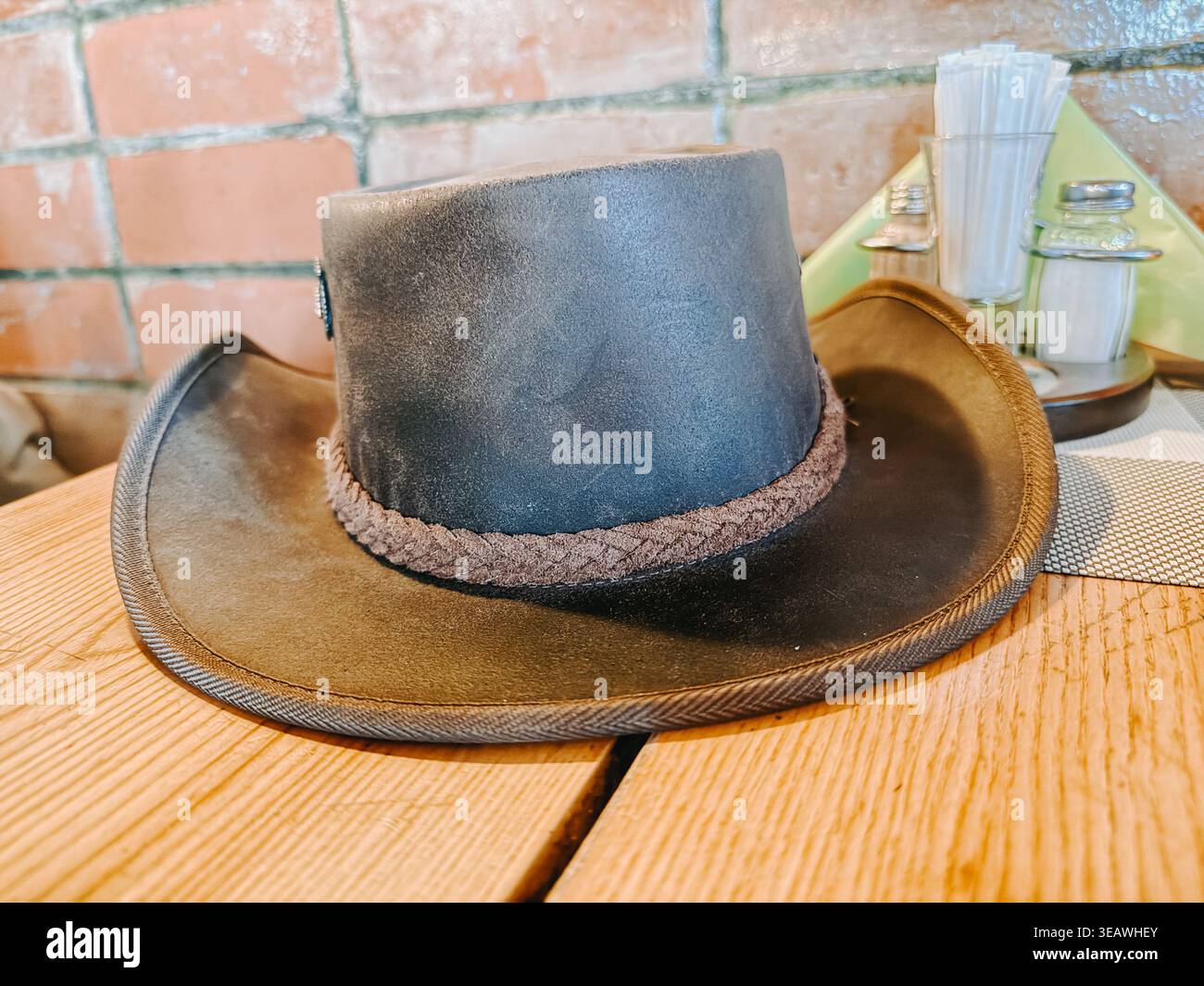 Valmiera, Lettland - 22. April 2026: Stilvoller Cowboyhut aus Leder auf einem Holztisch in einem gemütlichen rustikalen Café. Warme Töne und strukturierte Backgr Stockfoto
