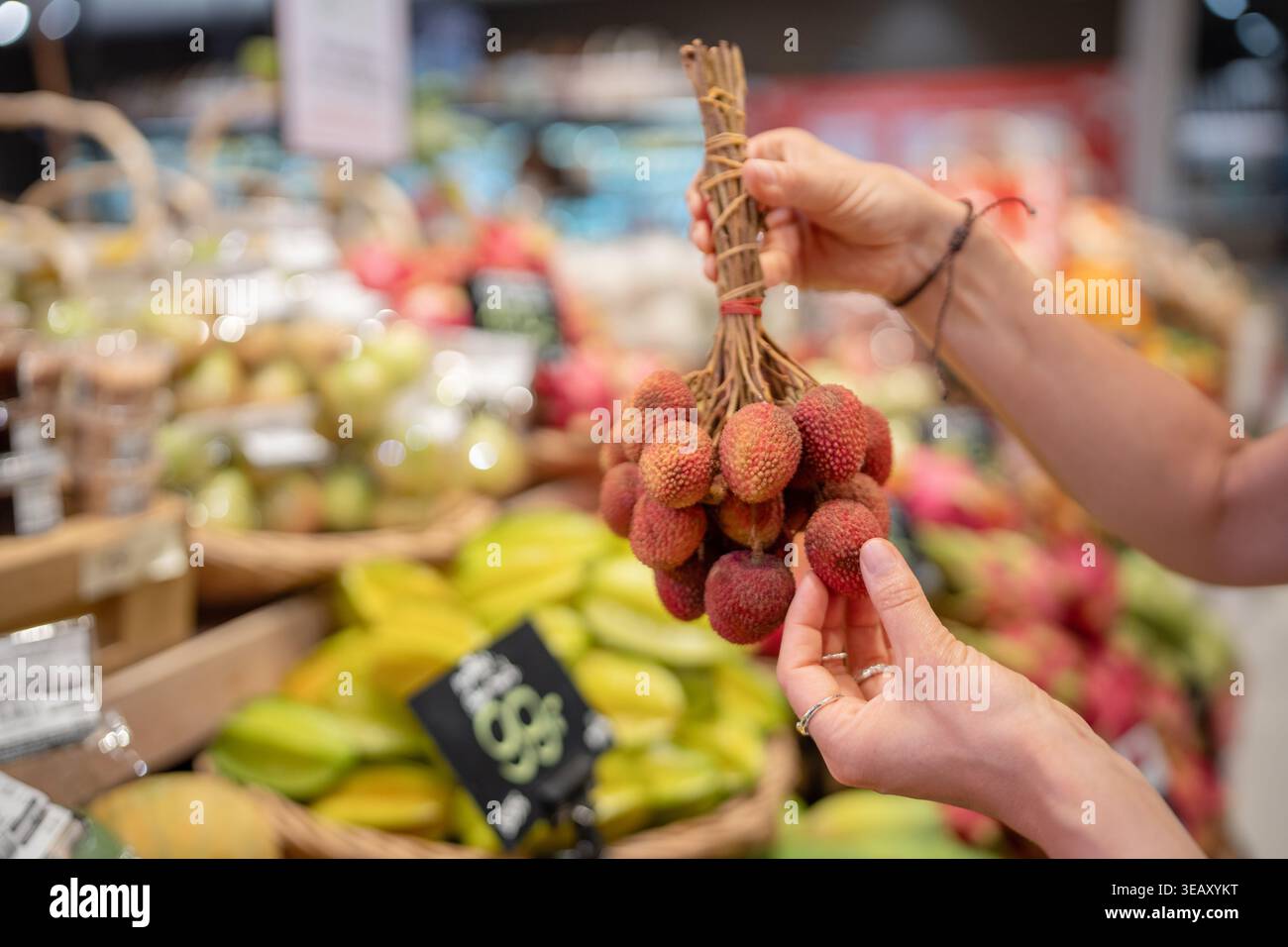 Eine Frau, die reife Litschi-Früchte im Supermarkt in Thailand auswählt und einen Haufen Früchte auf Zweigen hält. Stockfoto