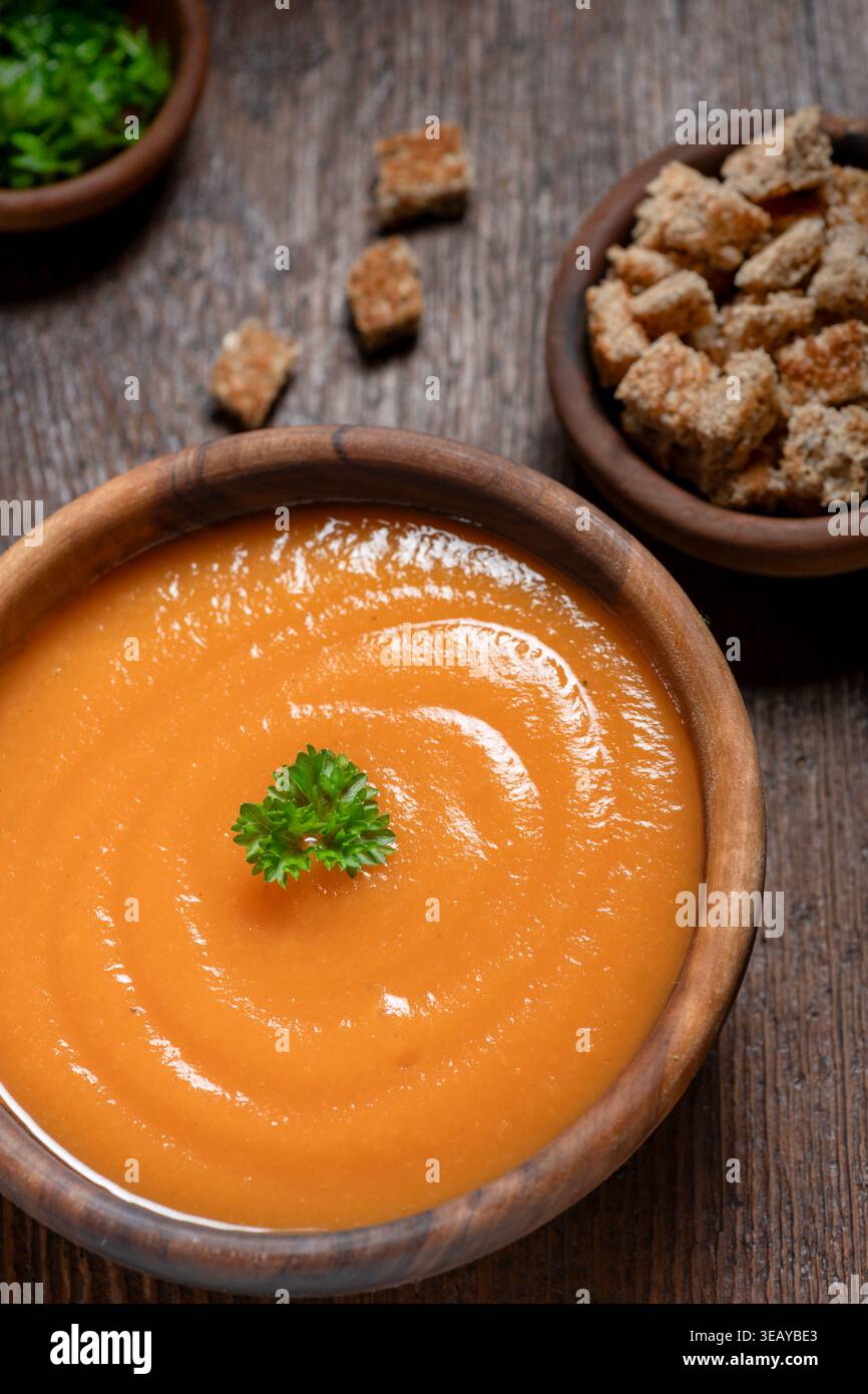 Eingeäscherte Karottensuppe auf einem rustikalen Holztisch Croutons an der Seite. Stockfoto