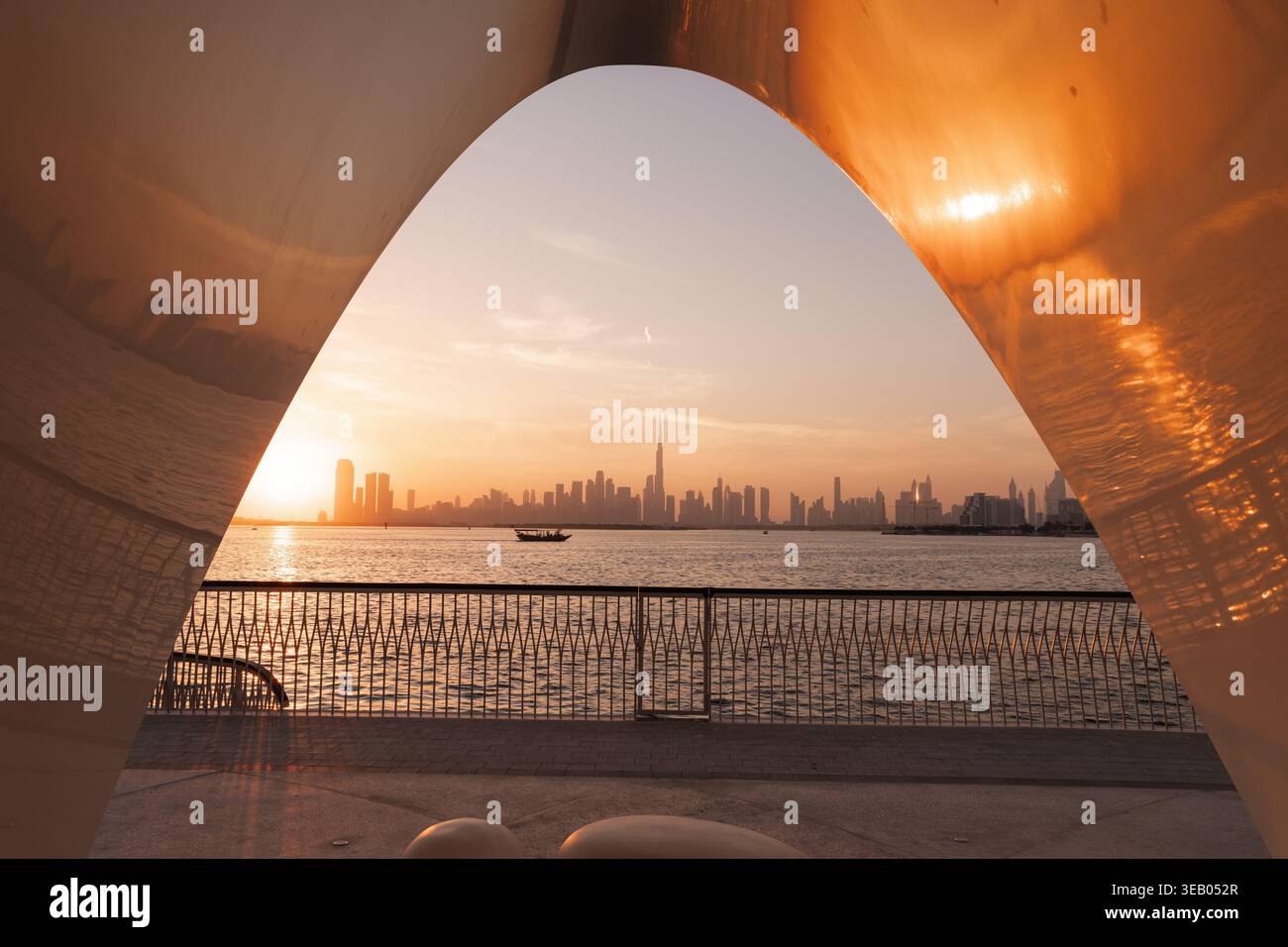 Sonnenuntergang in Dubai, während Sie in der Nähe einer Skulptur am Wasser stehen und die Skyline und die Lichter der Stadt betrachten. Stockfoto