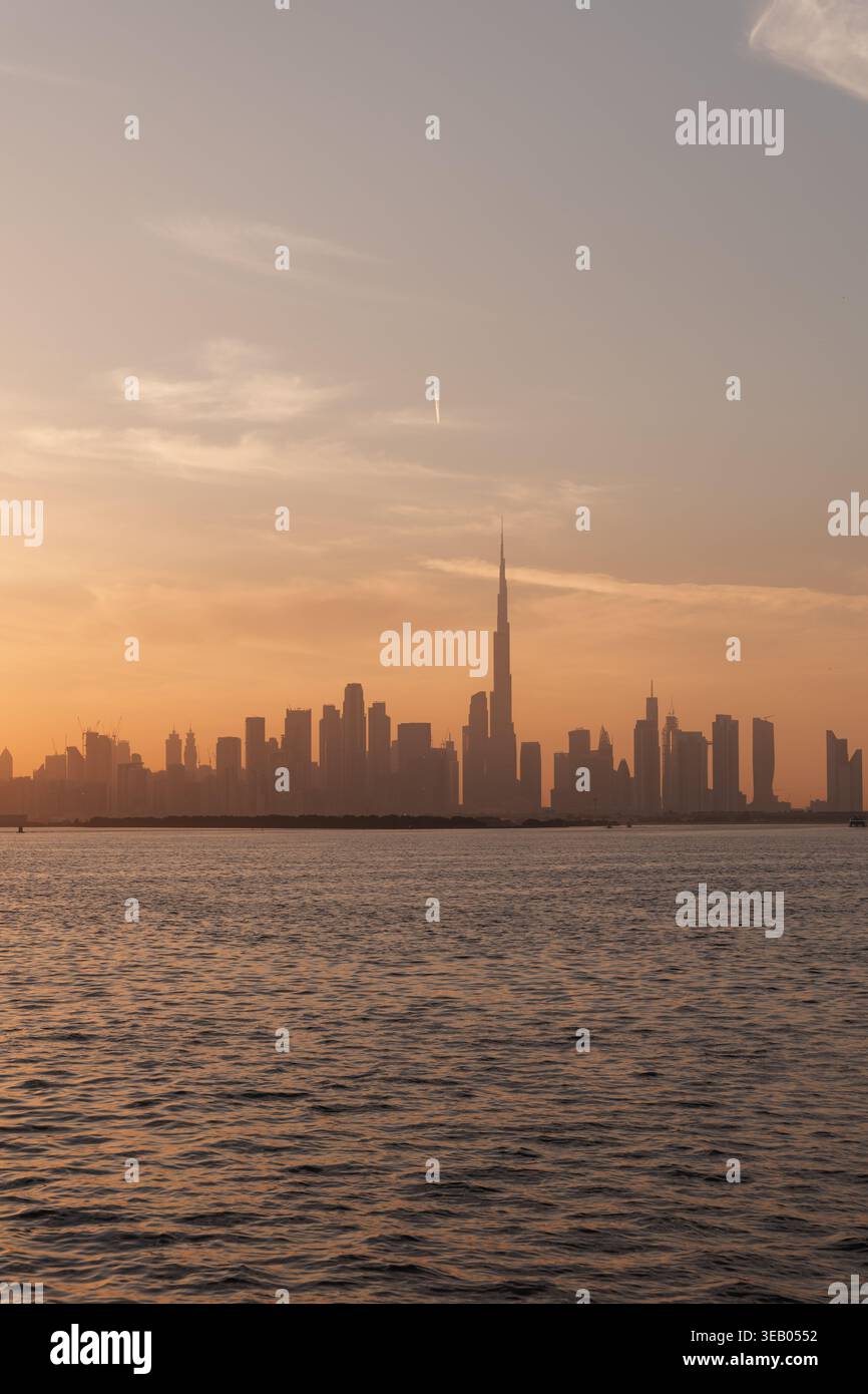 Der Sonnenuntergang erzeugt Schatten der Wolkenkratzer Dubais über ruhigem Wasser und hebt die berühmten Gebäude in der Skyline hervor, während der Himmel seine Farbe ändert. Stockfoto