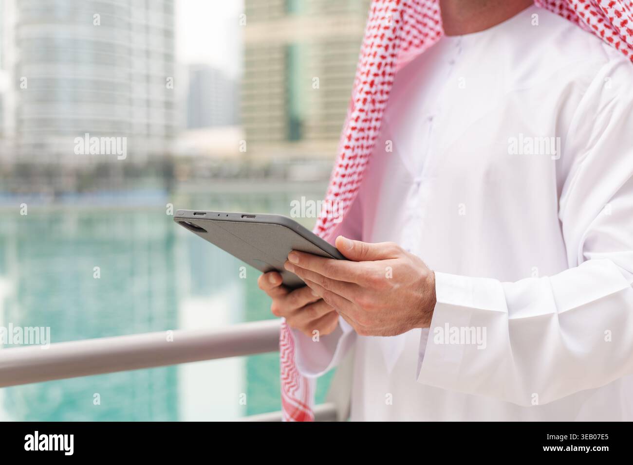 Ein arabischer Geschäftsmann steht in der Nähe des Wassers und hält eine Tafel, während er sich in einer städtischen Umgebung befindet. Die Gebäude der Stadt umgeben ihn. Stockfoto