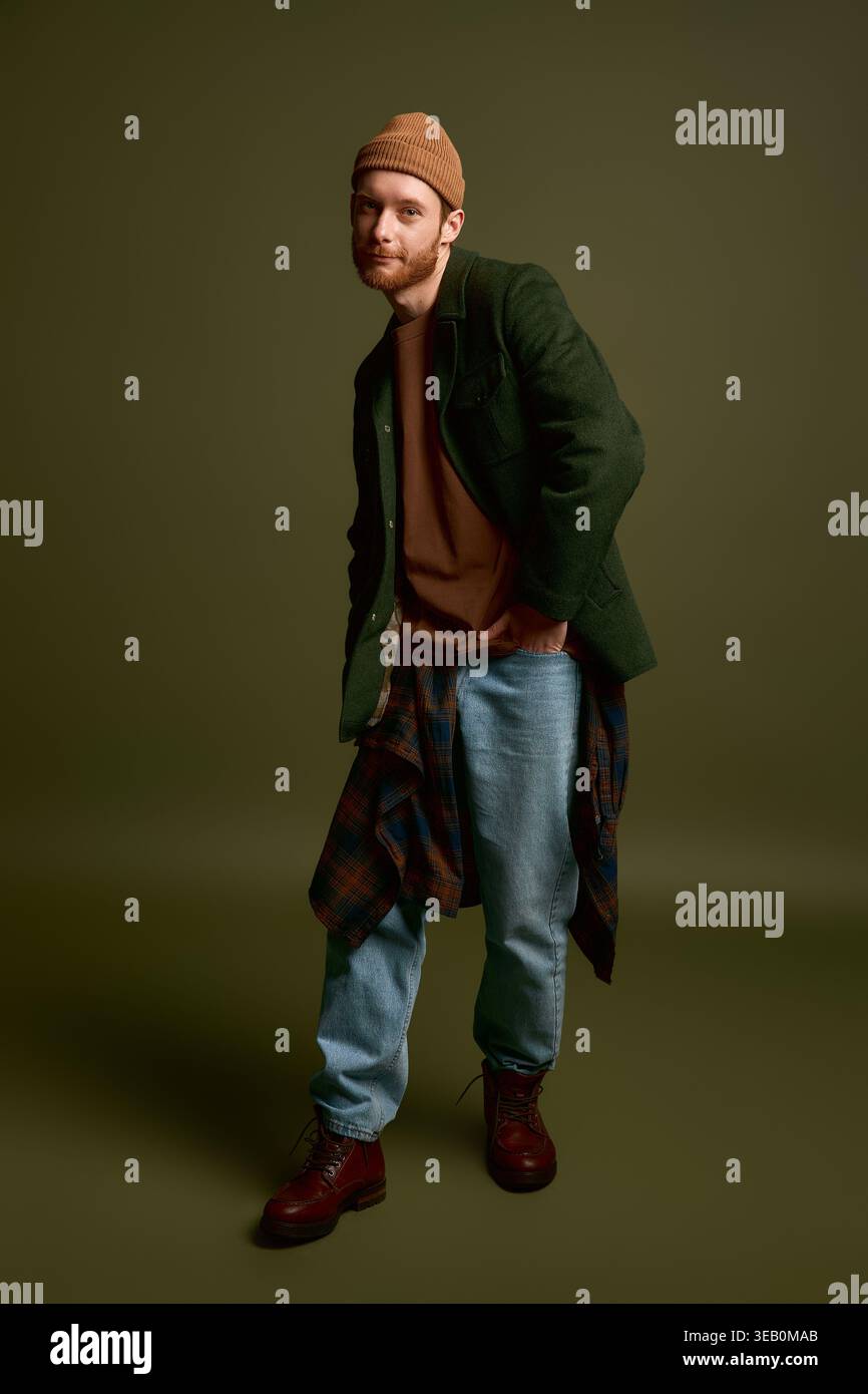 Ein junger Mann im trendigen Outfit posiert vor einem minimalistischen Hintergrund modisch. Stockfoto