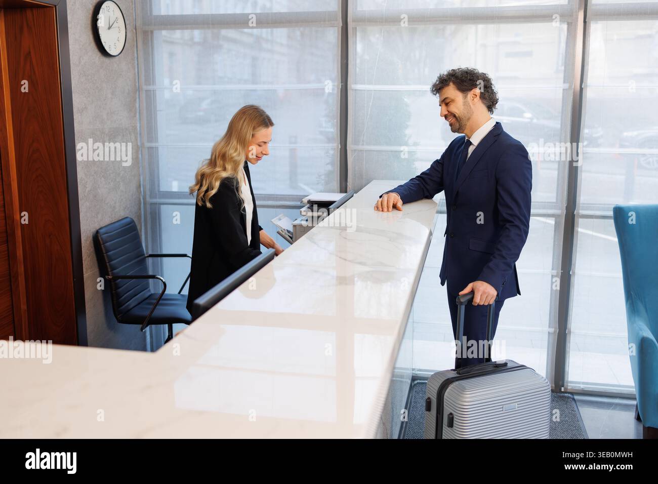 Geschäftsreisende warten an der Rezeption, während das Hotelpersonal Check-in-Dokumente vorbereitet Stockfoto