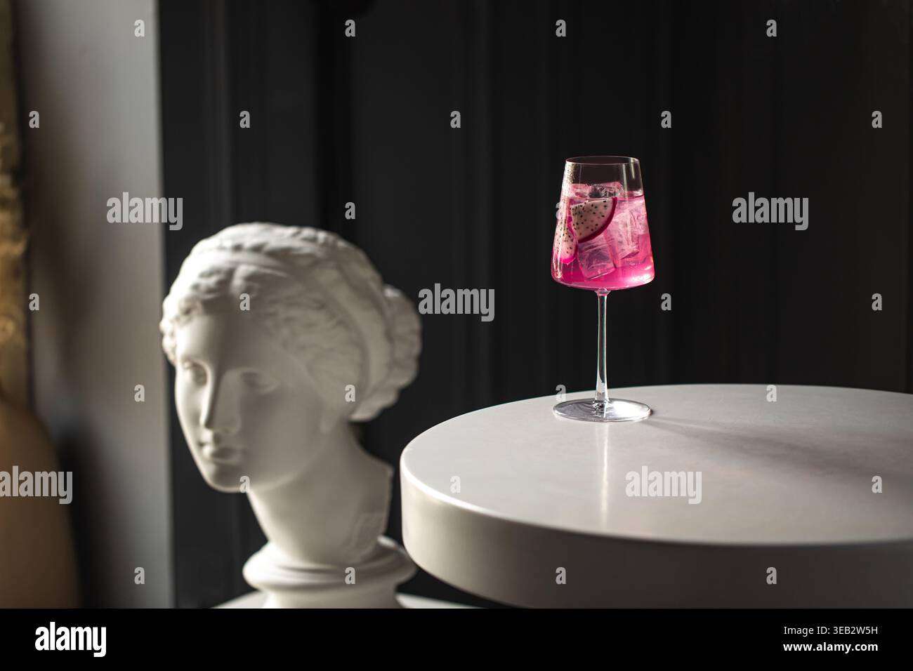 Rosafarbener Cocktail mit Obst auf dem Tisch und Statue Stockfoto