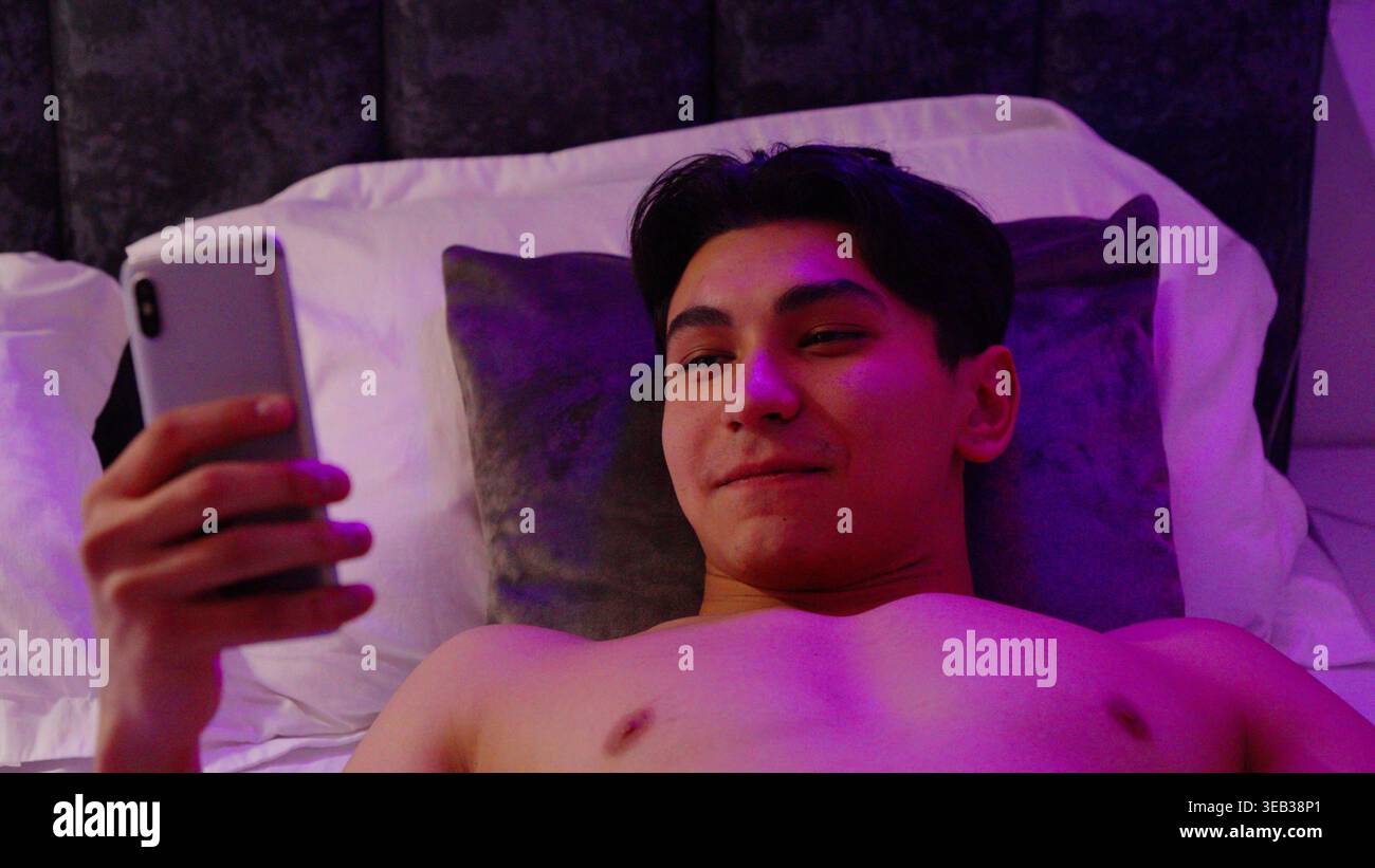 Mann, der ein Smartphone benutzt, während er nachts im Bett liegt Stockfoto