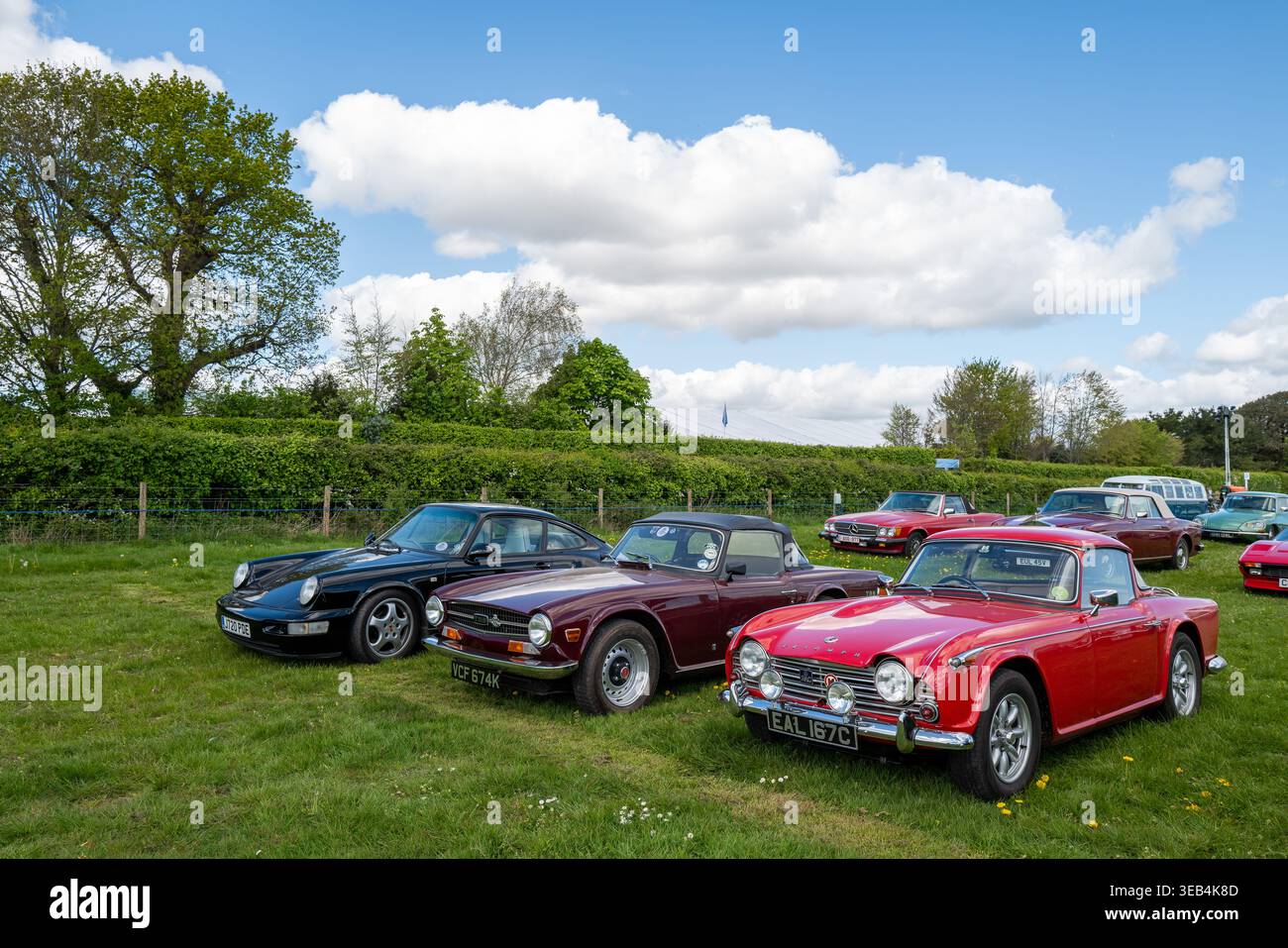 20. April: Zwei klassische Triumph TR's und ein Porsche auf dem Oldtimer- und Oldtimerparkplatz auf der Goodwood Race Circuit, West Sussex, England, Großbritannien. Stockfoto