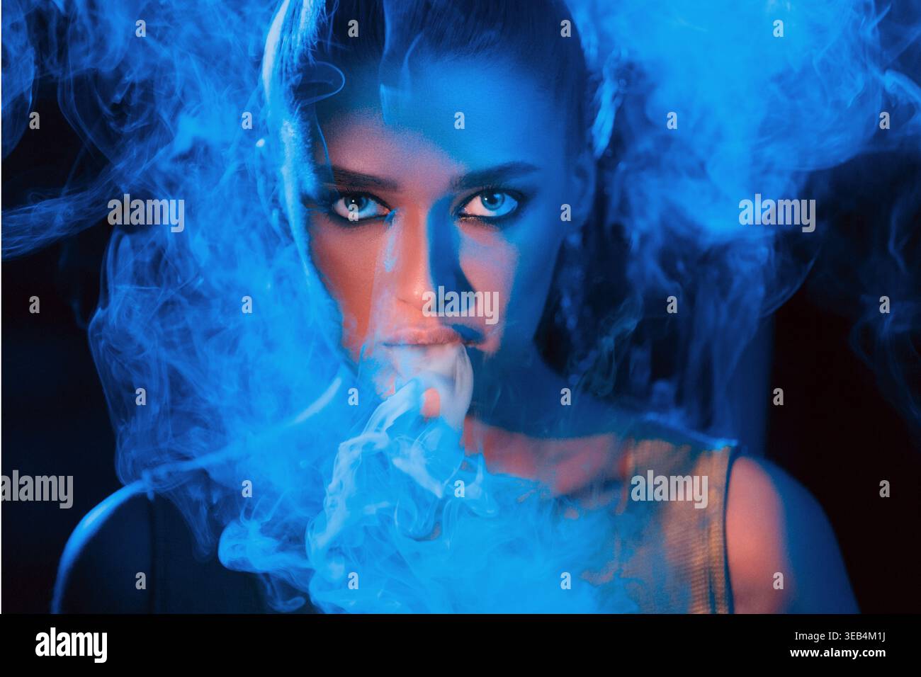 Frau, die während einer Creative Arts Session in leuchtendem Blaulicht Rauch ausatmet Stockfoto