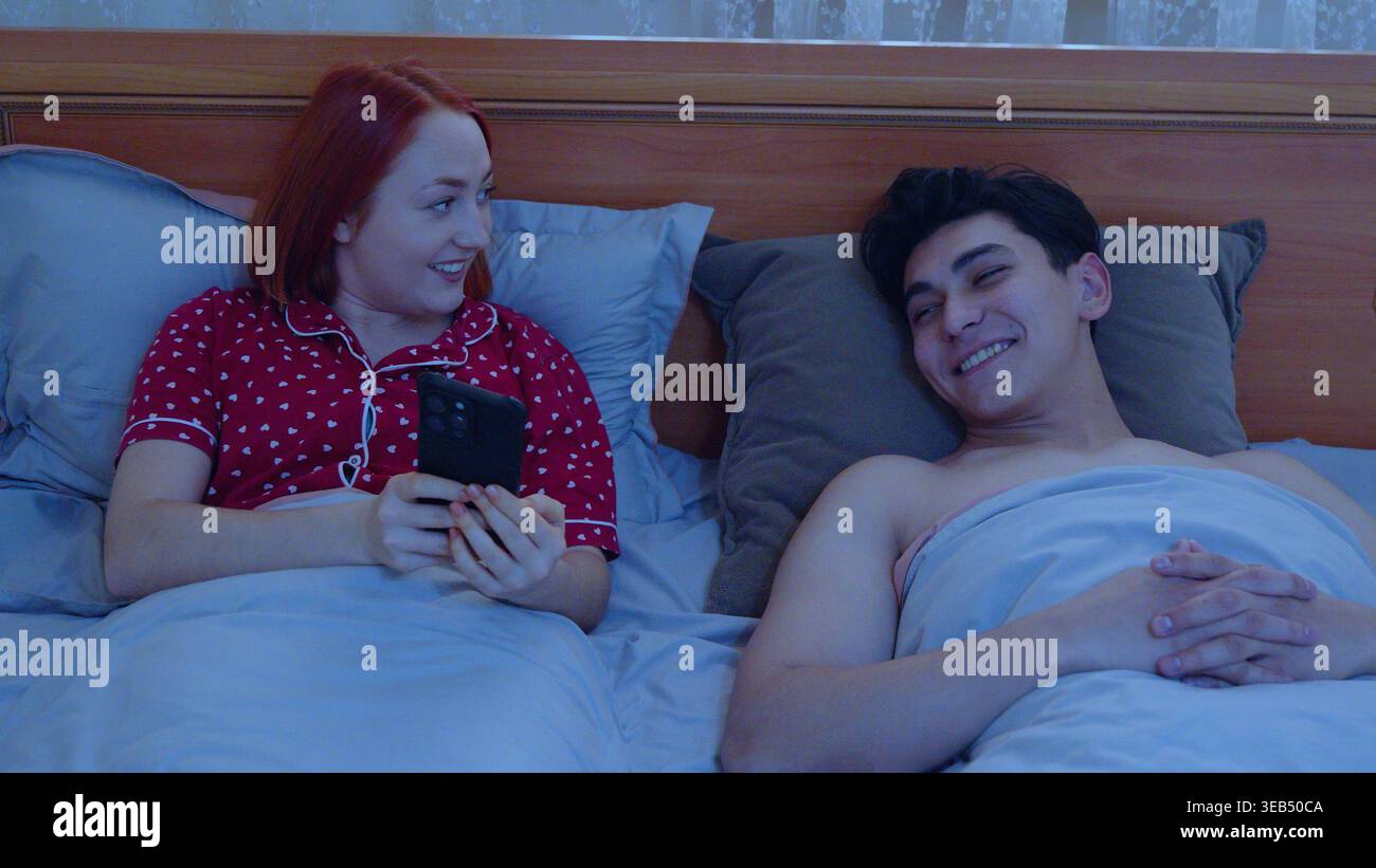Ein Paar, das im Bett liegt und ihr Smartphone benutzt Stockfoto