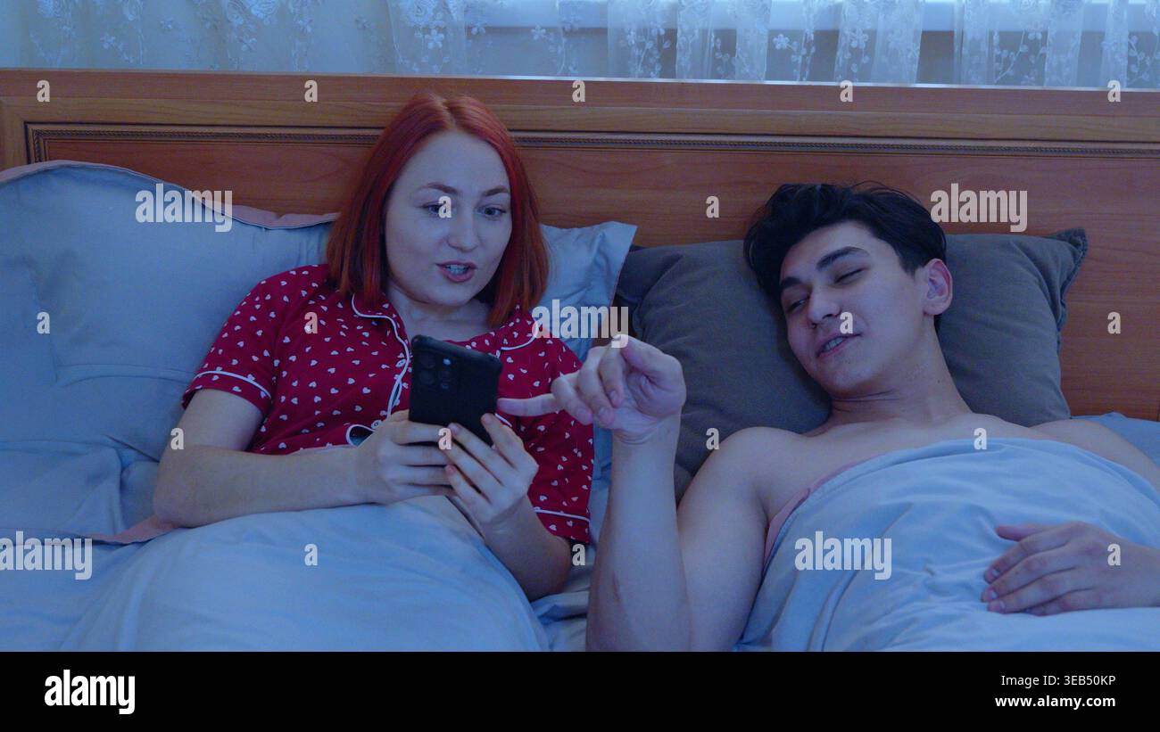 Pärchen im Bett mit Handys vor dem Schlafen Stockfoto