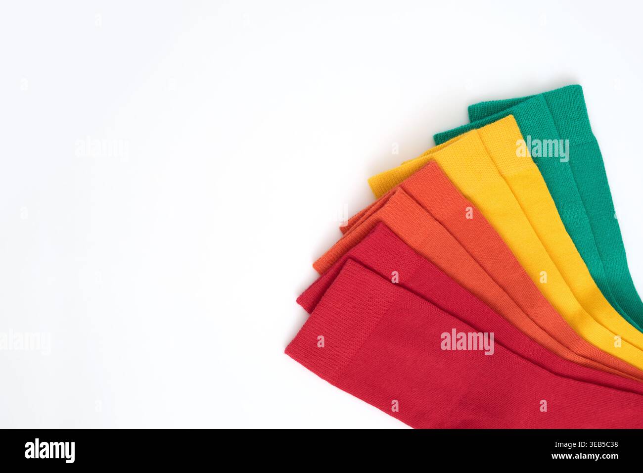 Bunte Socken, die ordentlich auf einer weißen Oberfläche angeordnet sind und ein Regenbogenspektrum zeigen Stockfoto