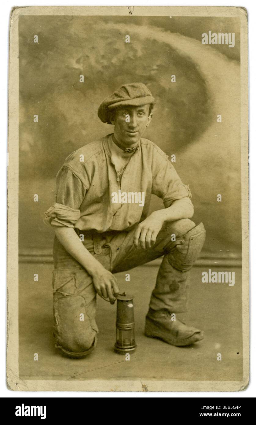 Postkarte aus den 1900er Jahren eines jungen Bergarbeiters mit flacher Kappe, Lampe, mit mobilem Studio-Hintergrund, von J Roberts, Leeds. Yorkshire, Großbritannien, um 1920 Stockfoto
