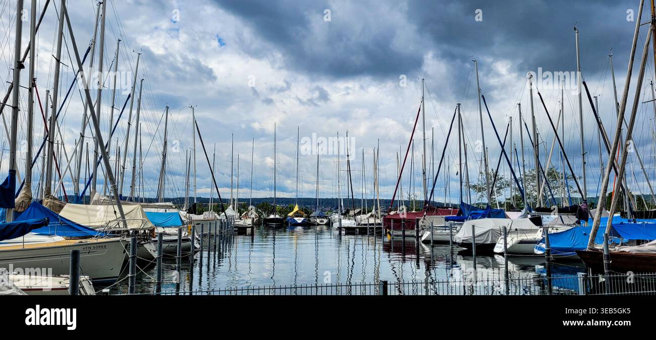 Uberlingen, Deutschland - 30. Juni 2024. Yachthafen mit Segelbooten, die am Pier vor einem dramatischen Himmel vertäut sind. Lineare Perspektive im Foto. Stockfoto