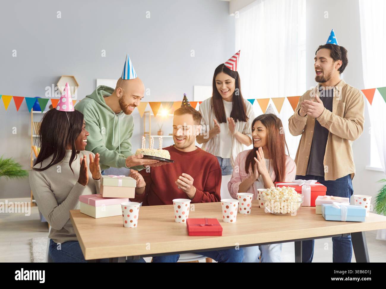Fröhliche Freunde gratulieren der Geburtstagsperson mit Kuchen, feiern Geburtstag zu Hause und klatschen. Stockfoto